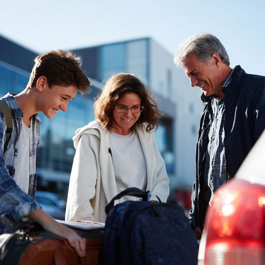 Happy parents helping their teenage son to get thing out of a car